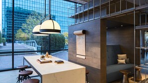 Ein modernes Interieur mit einem großen Fenster, einer zentralen Kochinsel mit Hockern, einer Couch und einer hängenden Leuchte.