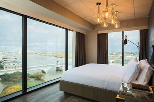 Habitación de hotel con una cama grande, una mesa de vidrio y vistas a un río y un puente.