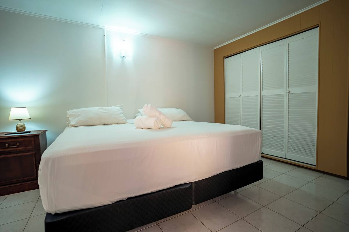 A neatly made bed with white linens, a bedside table with a lamp, and a large wardrobe with sliding doors.