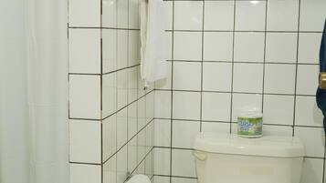 Ein Badezimmer mit Toilette, einer Duschvorhang, einem Handtuchhalter, einem Mülleimer und einer Flasche Flüssigseife.