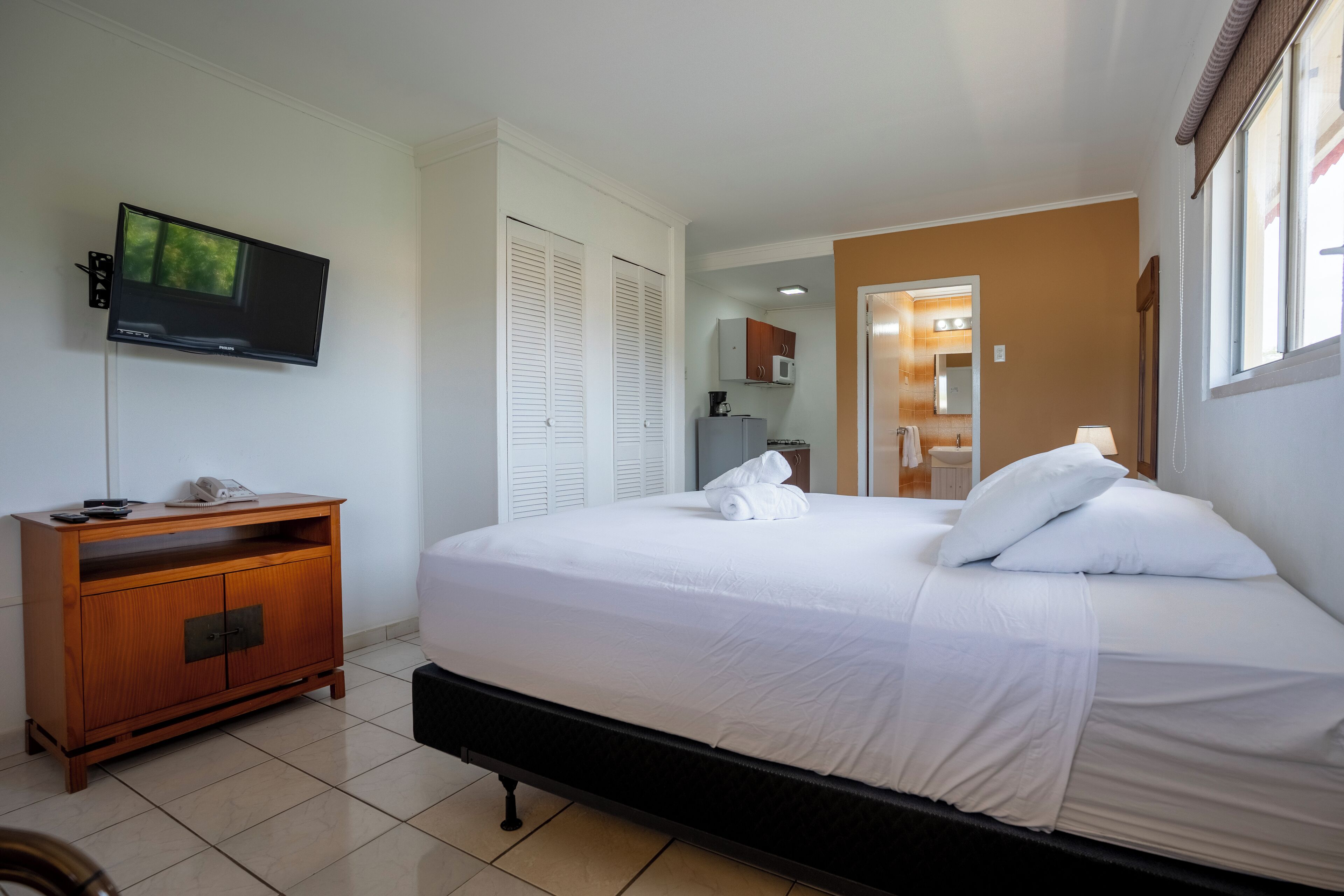 Habitación de hotel con cama, televisión, aparador de madera y baño a la vista a través de una puerta abierta.