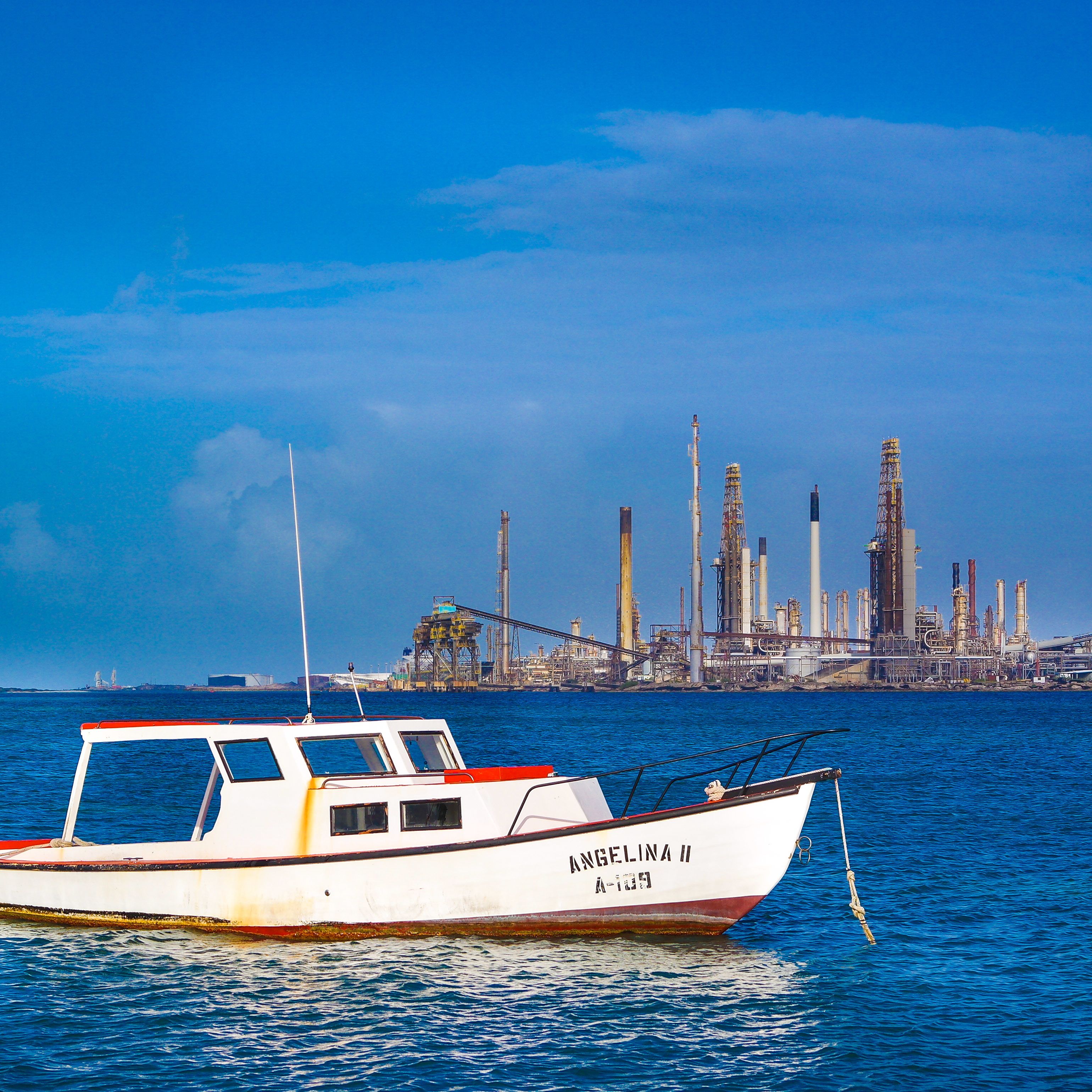 Un barco llamado 'Angelina II' en aguas tranquilas con un paisaje urbano industrial al fondo.