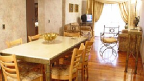 A dining area with a long table and chairs, a television, and a statue. - Reina Victoria Suites & Towers (Mendoza)