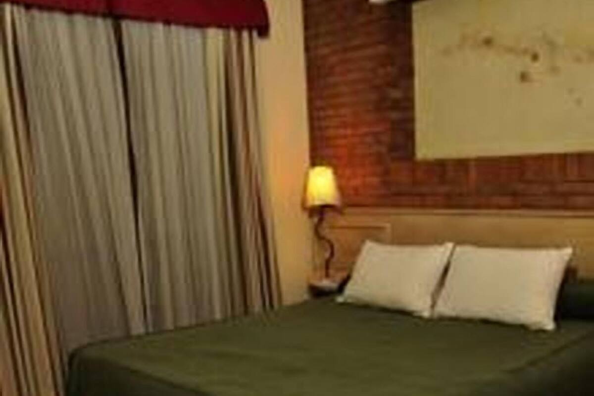 A hotel room with a large bed, wooden flooring, a red curtain, and a wall-mounted lamp.