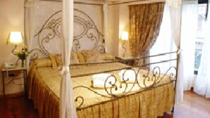 A four-poster canopy bed with a decorative headboard, a bedside table with a lamp, and a view of the outdoors through a window with curtains. - Reina Victoria Suites & Towers (Mendoza)