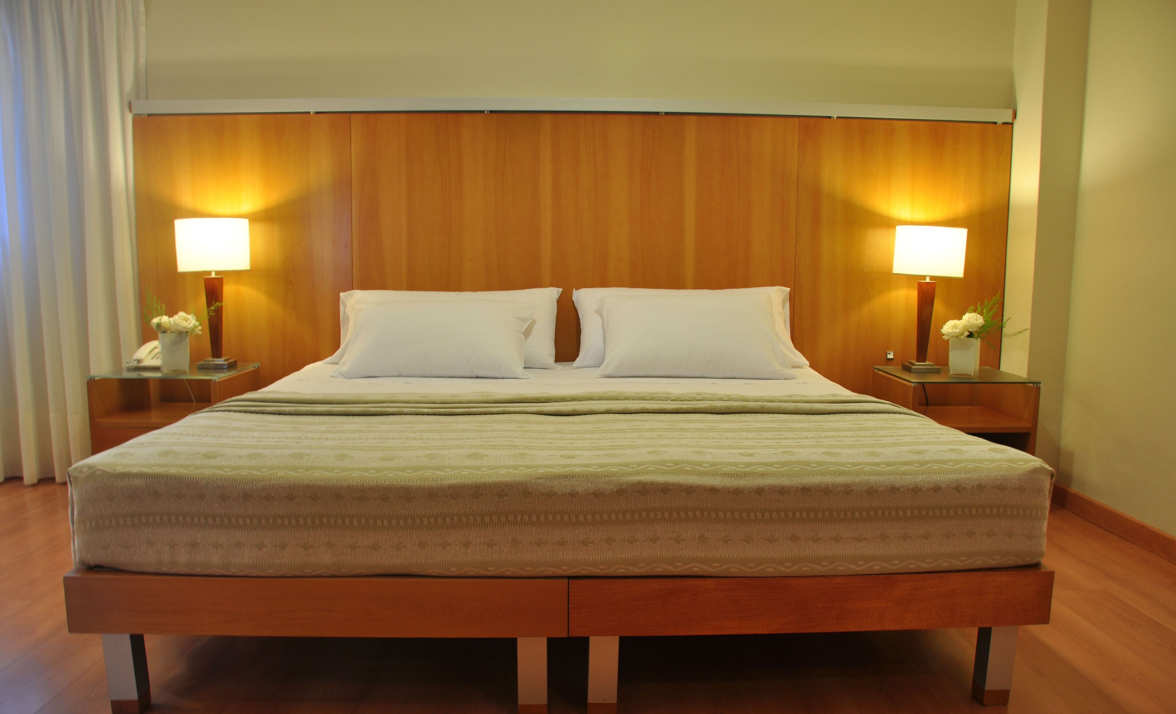 Quarto de hotel com uma cama grande, duas luminárias de cabeceira e um painel de cama de madeira.