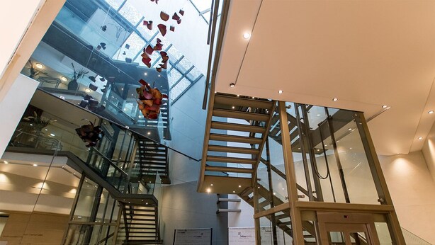 Un intérieur moderne avec un escalier en verre, un coin salon et une vue sur le ciel.