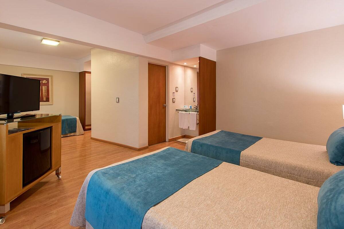 A hotel room with two beds, a TV, a desk, and a bathroom.