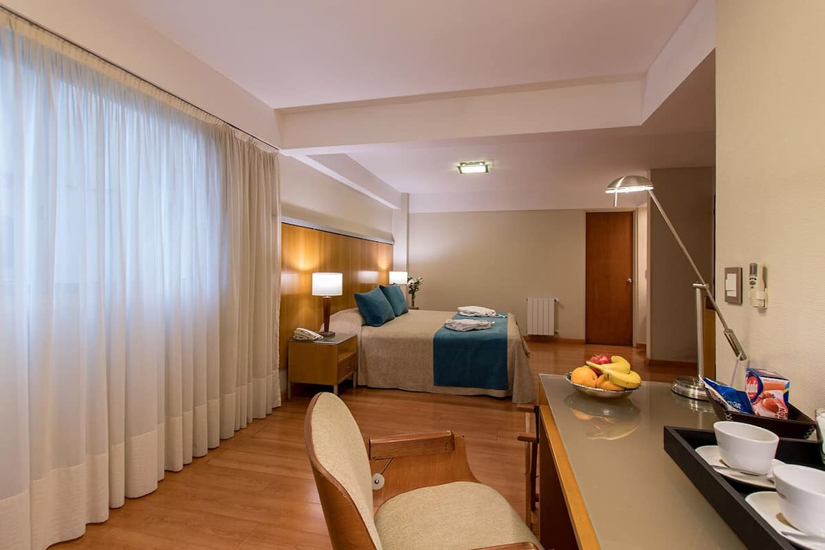 A hotel room with a bed, bedside table, lamp, and a breakfast tray with fruits.