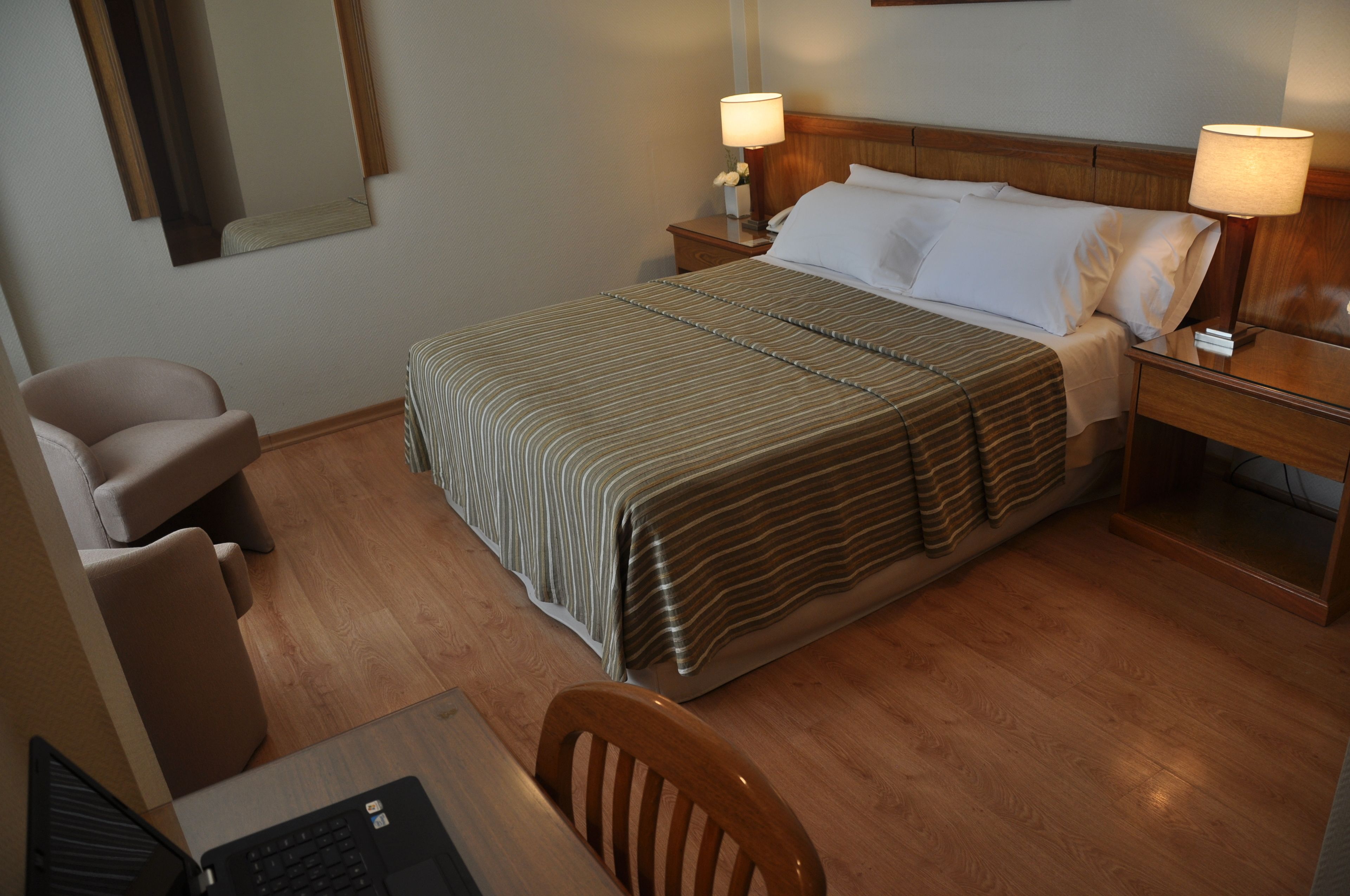 Une chambre d’hôtel comprenant un lit, deux tables de chevet, un bureau avec une chaise et un ordinateur portable.