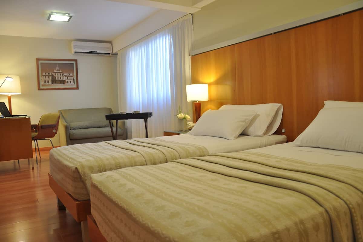 A hotel room with two beds, a desk, a chair, a lamp, and a framed picture on the wall.