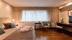 Une chambre d’hôtel avec un lit, un bureau, une chaise et une fenêtre avec des rideaux.