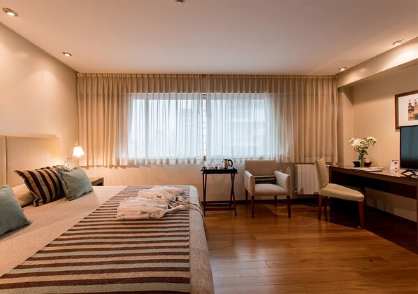 A hotel room with a bed, a desk, a chair, and a window with curtains.