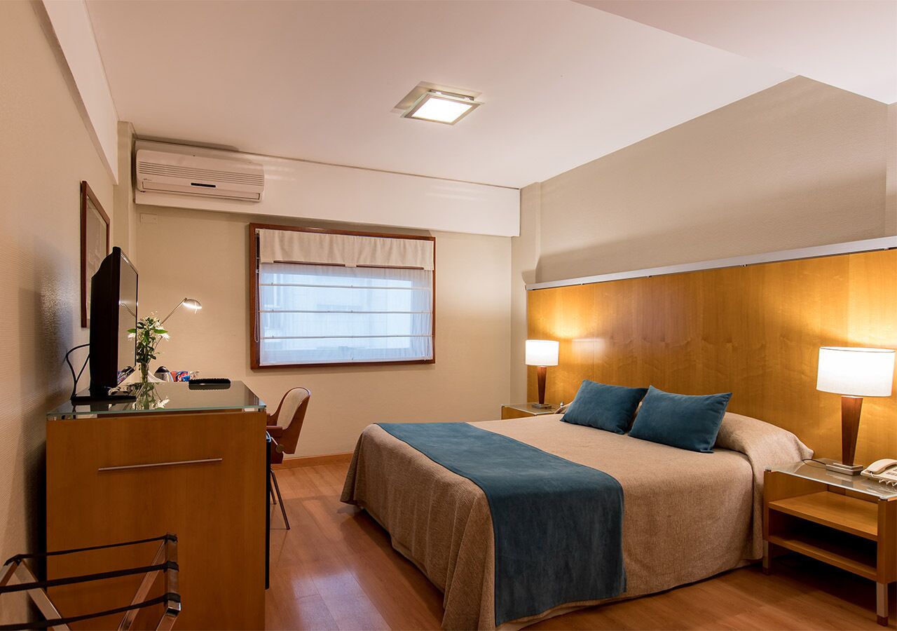 Habitación de hotel con cama, escritorio, silla y lámparas de noche.