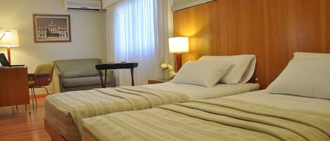 A hotel room with two beds, a desk, a chair, and a framed picture on the wall.