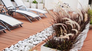 Un espace extérieur ensoleillé, aménagé avec des fauteuils confortables et un jardinier où poussent de hautes graminées.