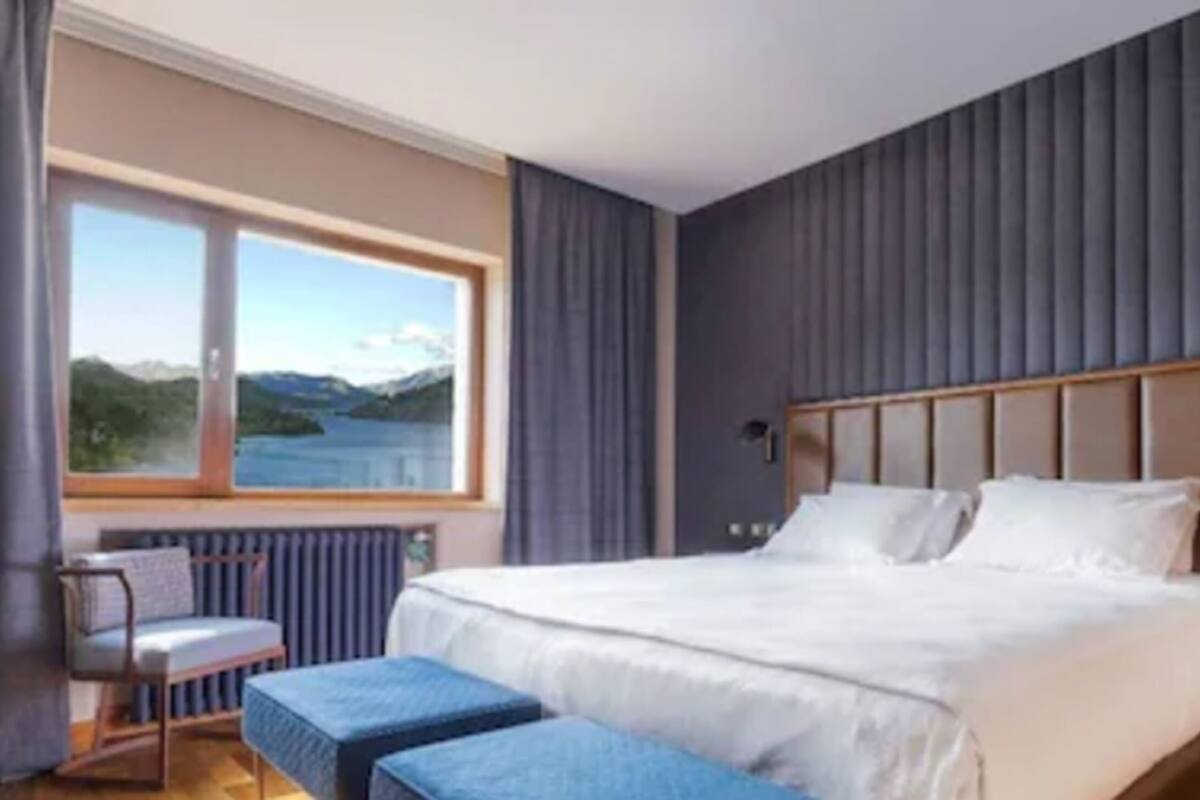 A hotel room with a large bed, a view of the outdoors, a small table, and a chair.