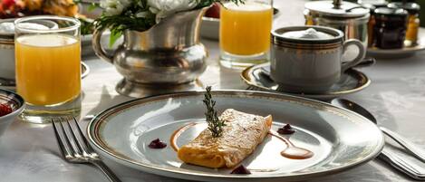 A breakfast setting with a plate of food, a glass of orange juice, a cup of coffee, and a pitcher of flowers.