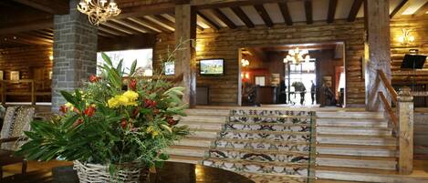 A lobby with a wooden staircase, a chandelier, and a floral arrangement on a table.