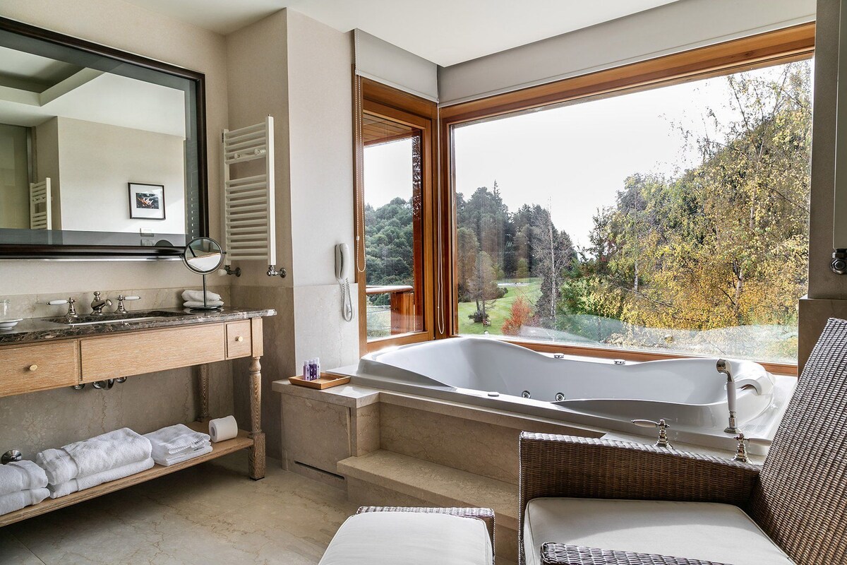 Ein modernes Badezimmer mit einer großzügigen Badewanne, einem Holzbadezimmer-Möbel und Blick auf einen Wald durch ein großes Fenster.