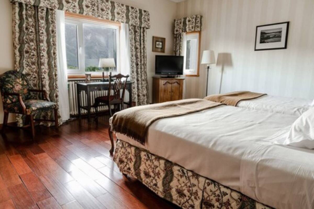 A hotel room with a large bed, a desk with a chair, a television, and a window with curtains.