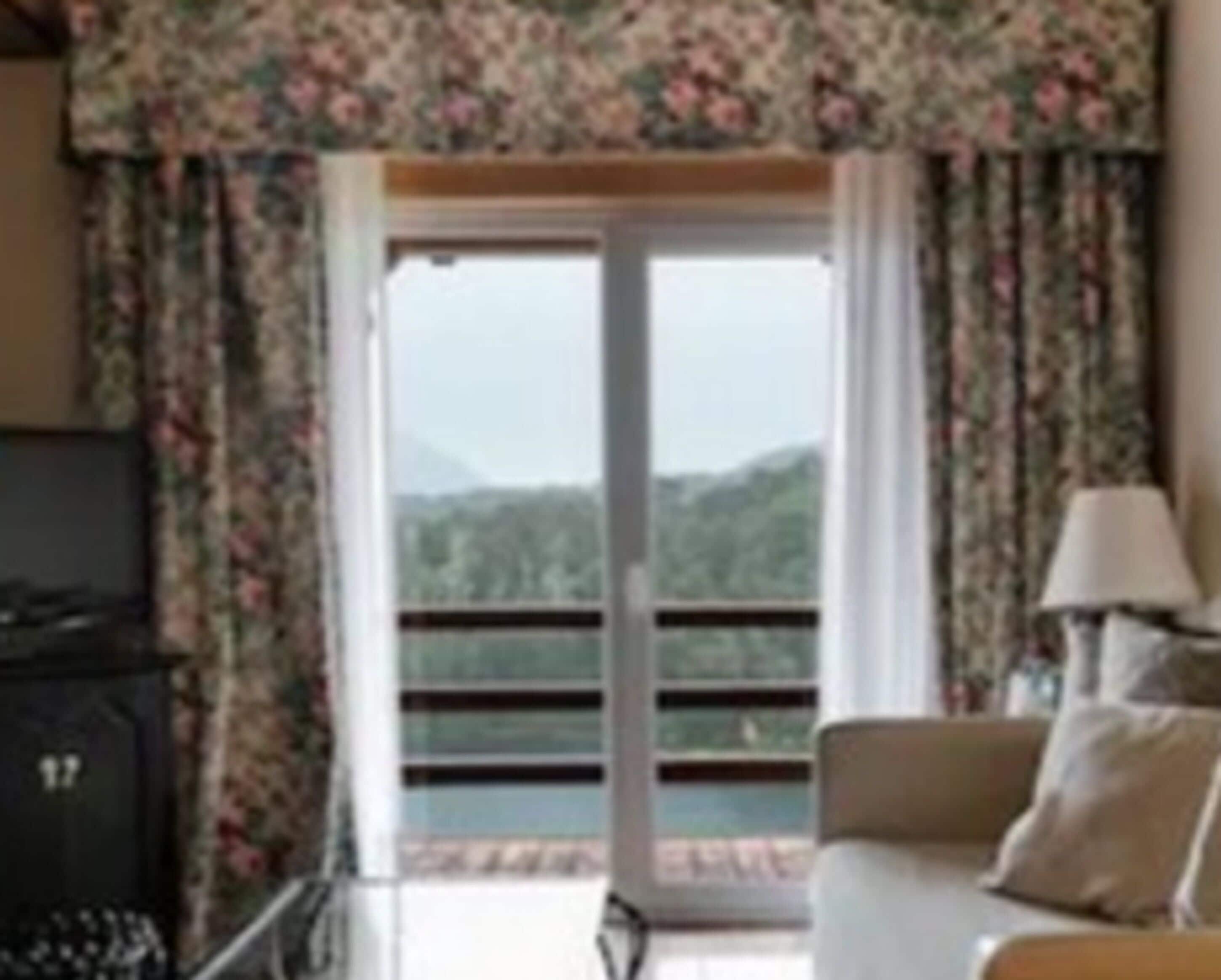 Une pièce comprenant un canapé, une lampe et donnant sur un paysage montagneux grâce à une porte vitrée.