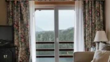 Une pièce comprenant un canapé, une lampe et donnant sur un paysage montagneux grâce à une porte vitrée.