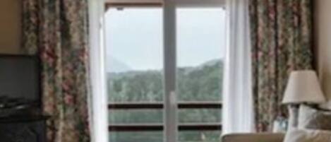 Una habitación con sofá, una lámpara y vista a un paisaje montañoso a través de un ventanal.