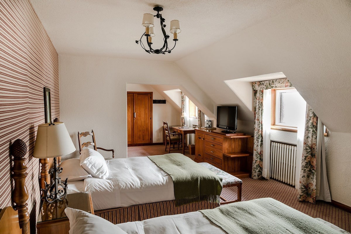 A hotel room with two beds, a desk, a television, and a window with curtains.
