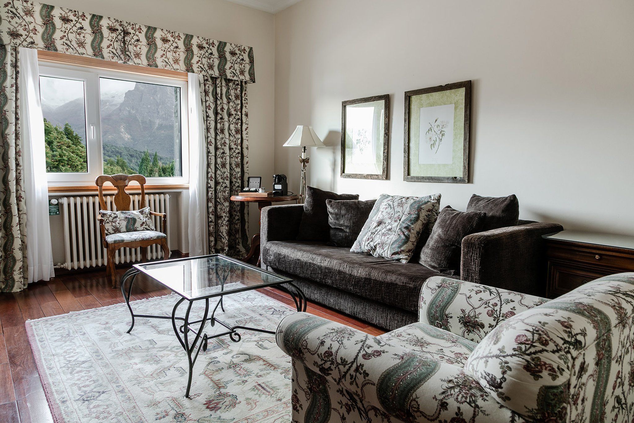 A cozy living room with a sofa, armchairs, a glass coffee table, and a view of mountains through a window.