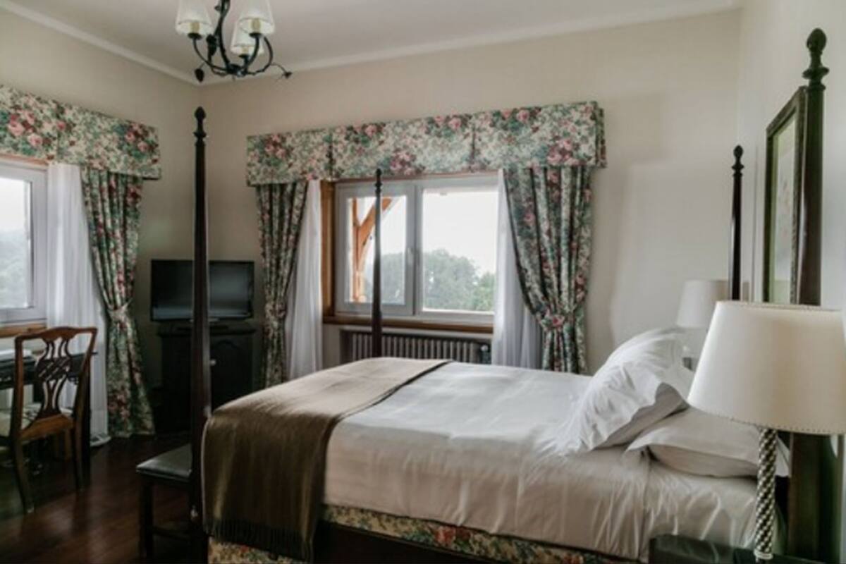A bedroom with a bed, a desk, a television, and a window with curtains.