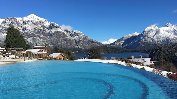 Un resort con piscina, cabañas de madera y montañas al fondo.