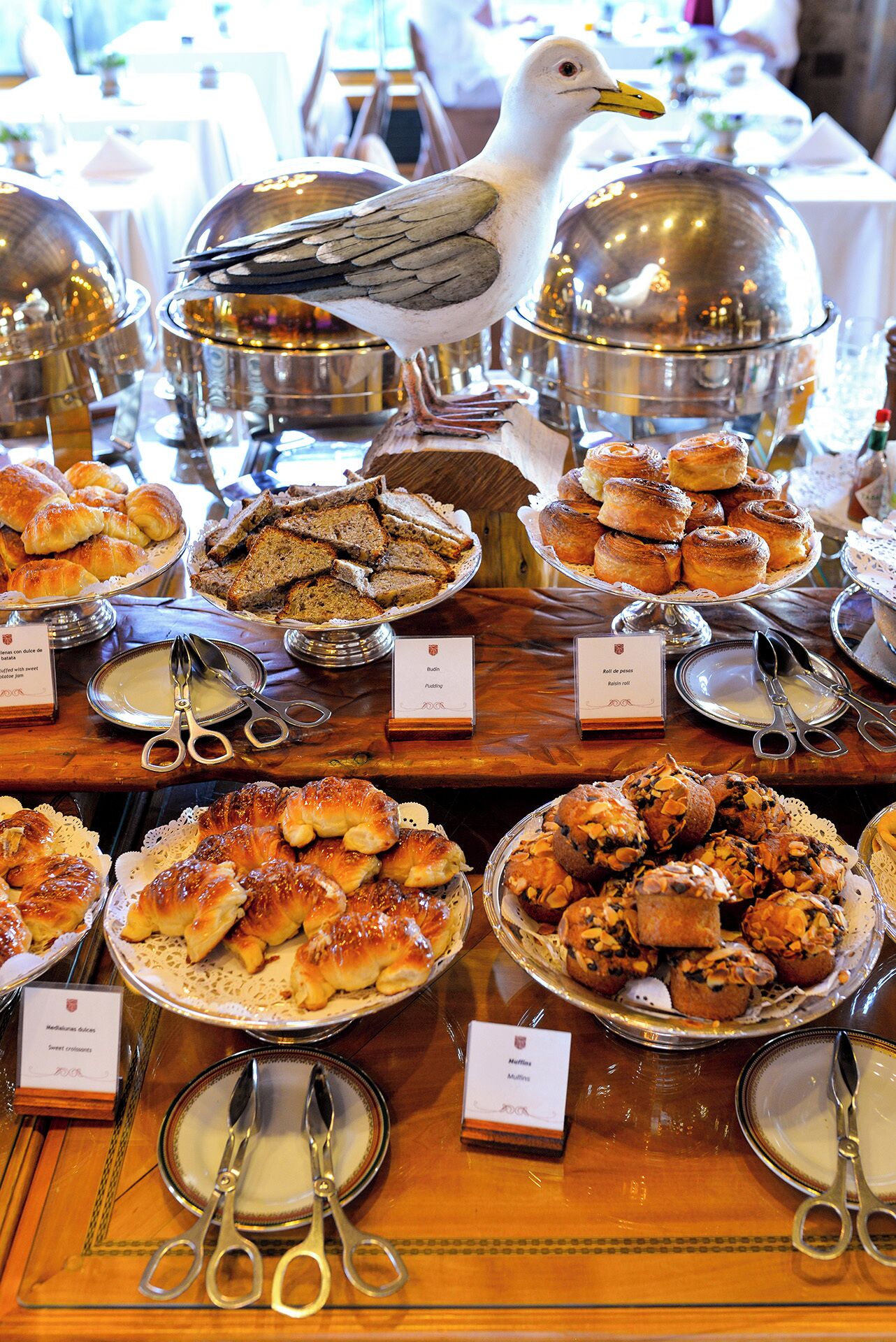 A buffet table with various pastries and desserts, including croissants, muffins, and rolls, labeled with their names.