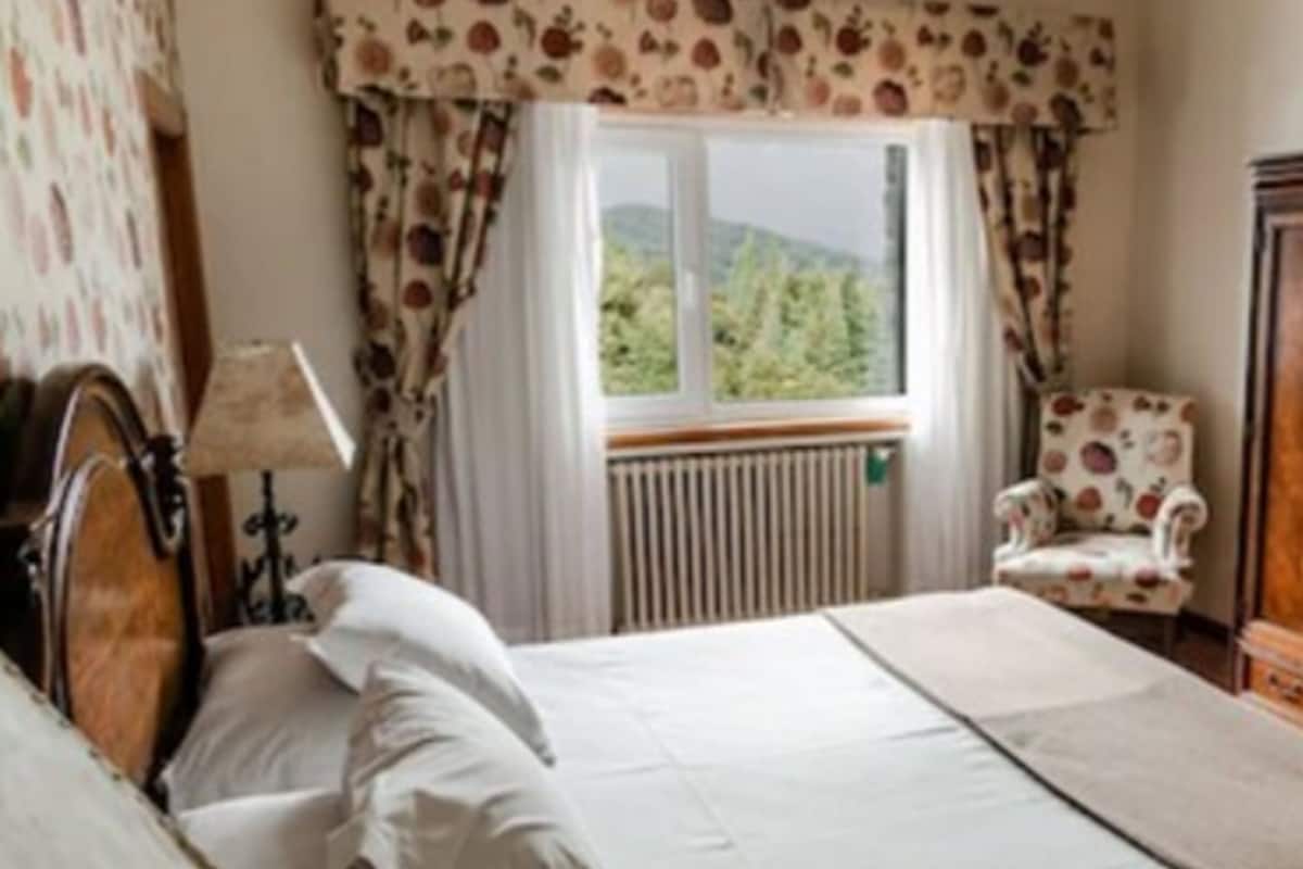 A bedroom with a bed, a chair, a lamp, and a window with curtains.