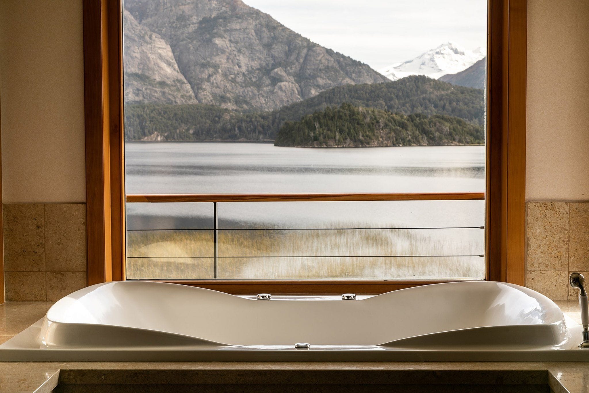 Un baño con bañera y ventana con vistas a un lago y montañas.