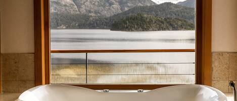Un baño con bañera y ventana con vistas a un lago y montañas.