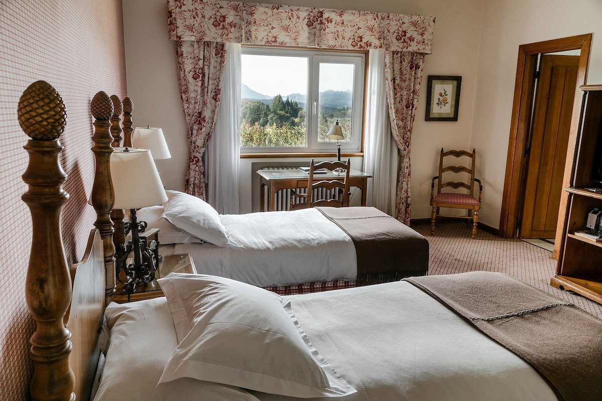 Une chambre avec deux lits, un bureau, une chaise et une fenêtre donnant sur l’extérieur.
