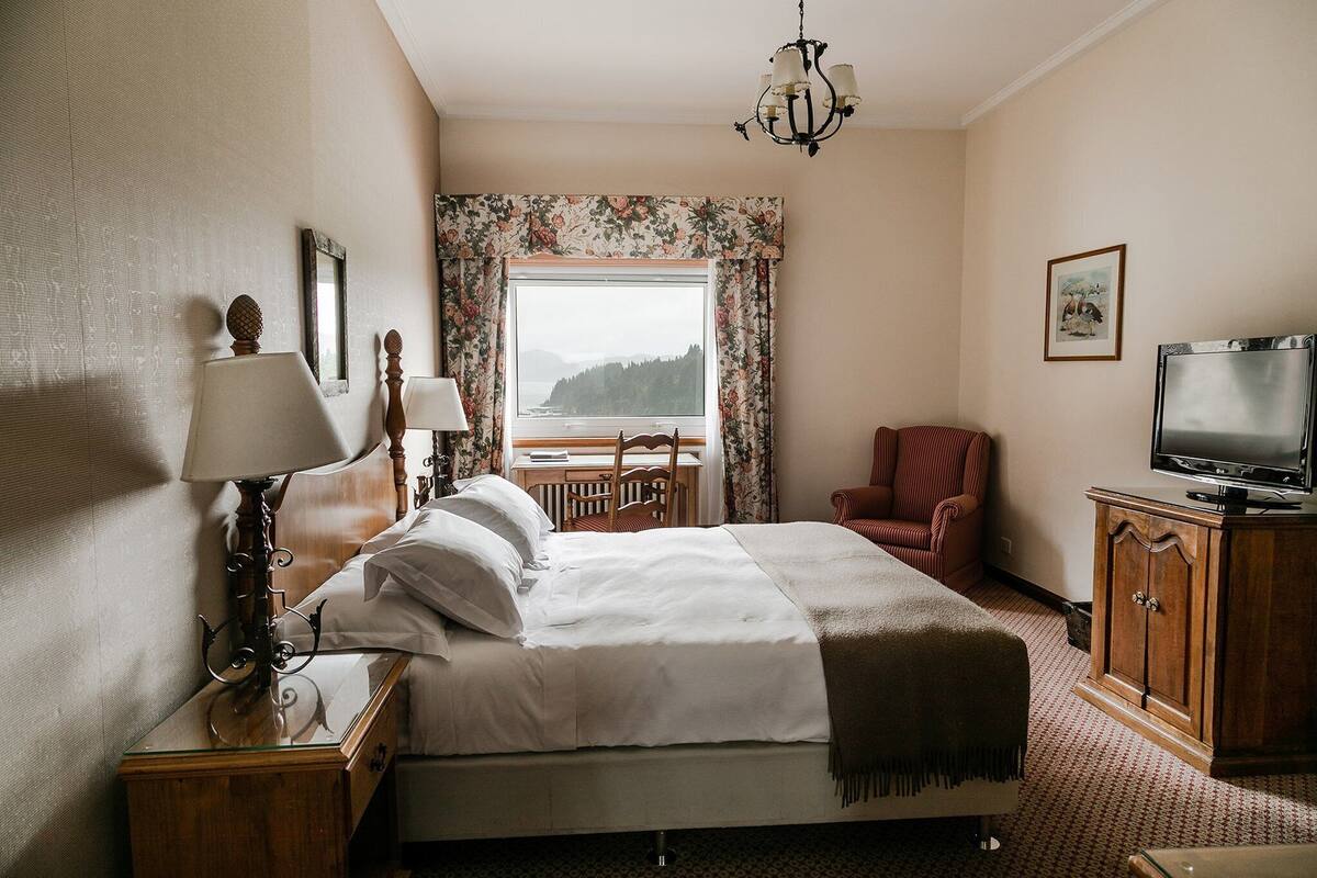 A hotel room with a bed, a desk, a chair, a television, and a view of the outdoors.