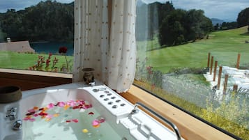 Ein Badezimmer mit einer Badewanne, gefüllt mit Rosenblättern, einem Fenster mit Blick auf eine grüne Landschaft und ein Gewässer.