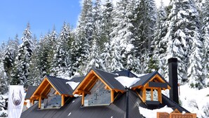 A snow-covered lodge with a stone facade, wooden beams, and a chimney. - Llao Llao Resort Golf & Spa (San Carlos de Bariloche)