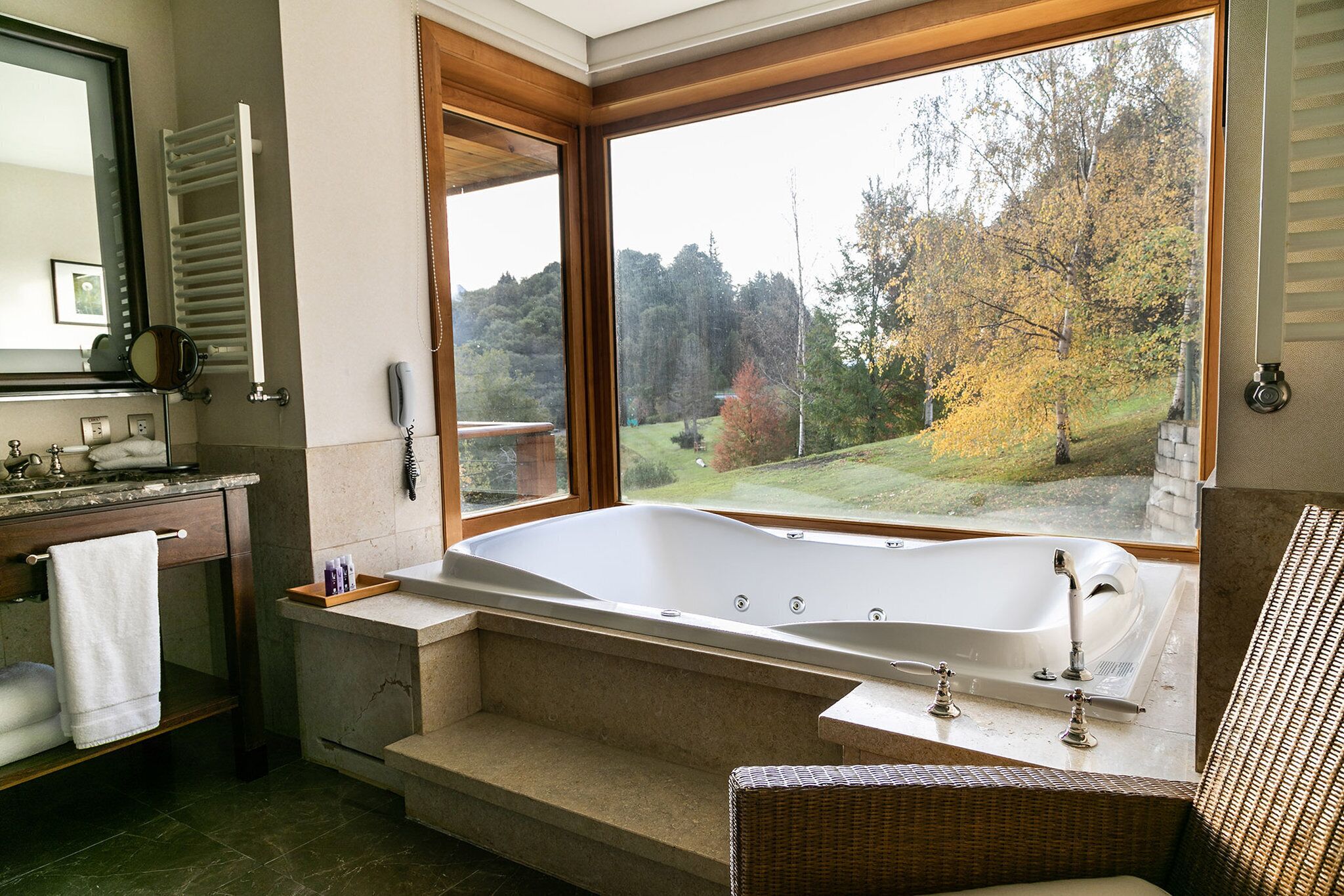 A bathroom with a large bathtub, a wooden-framed window, and a view of a forest.