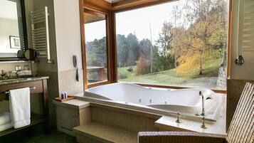 A bathroom with a large bathtub, a wooden-framed window, and a view of a forest.