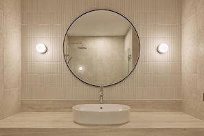 Un baño con un espejo redondo, un lavamanos y dos luces fijadas a la pared.