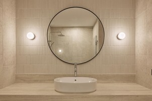 Un baño con un espejo redondo, un lavamanos y dos luces fijadas a la pared.