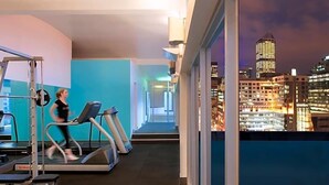 A gym with treadmills and weight machines, a cityscape view through large windows, and a modern interior design. - Flagstaff Gardens Hotel Melbourne (Melbourne)