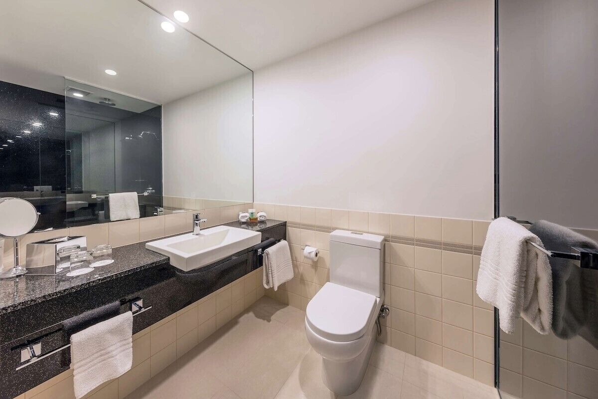 A modern bathroom with a sink, mirror, toilet, and towel rack.