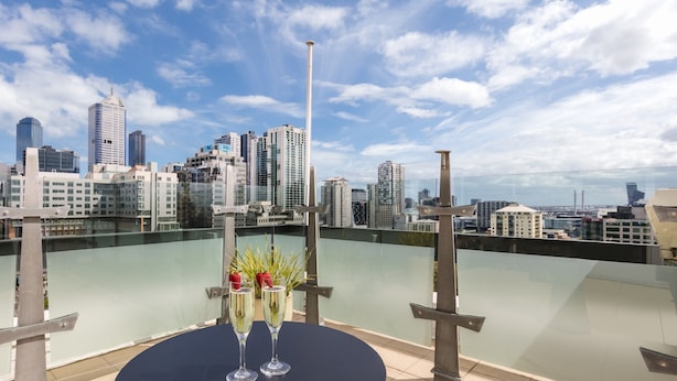A rooftop terrace with a city skyline view, a round table with two champagne flutes, and a glass railing. - Flagstaff Gardens Hotel Melbourne (Melbourne)
