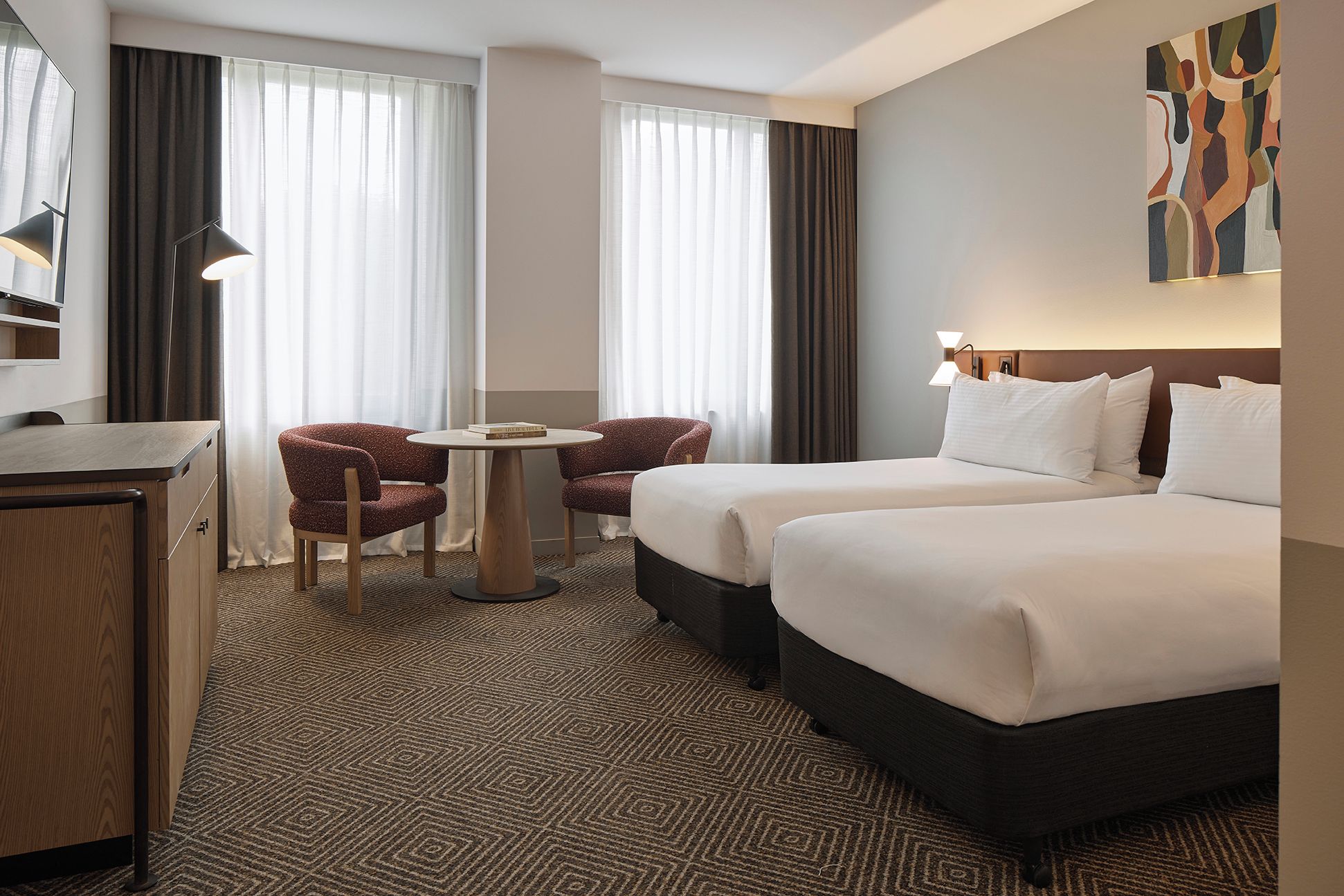 A hotel room with two beds, a desk, a chair, and a small table.