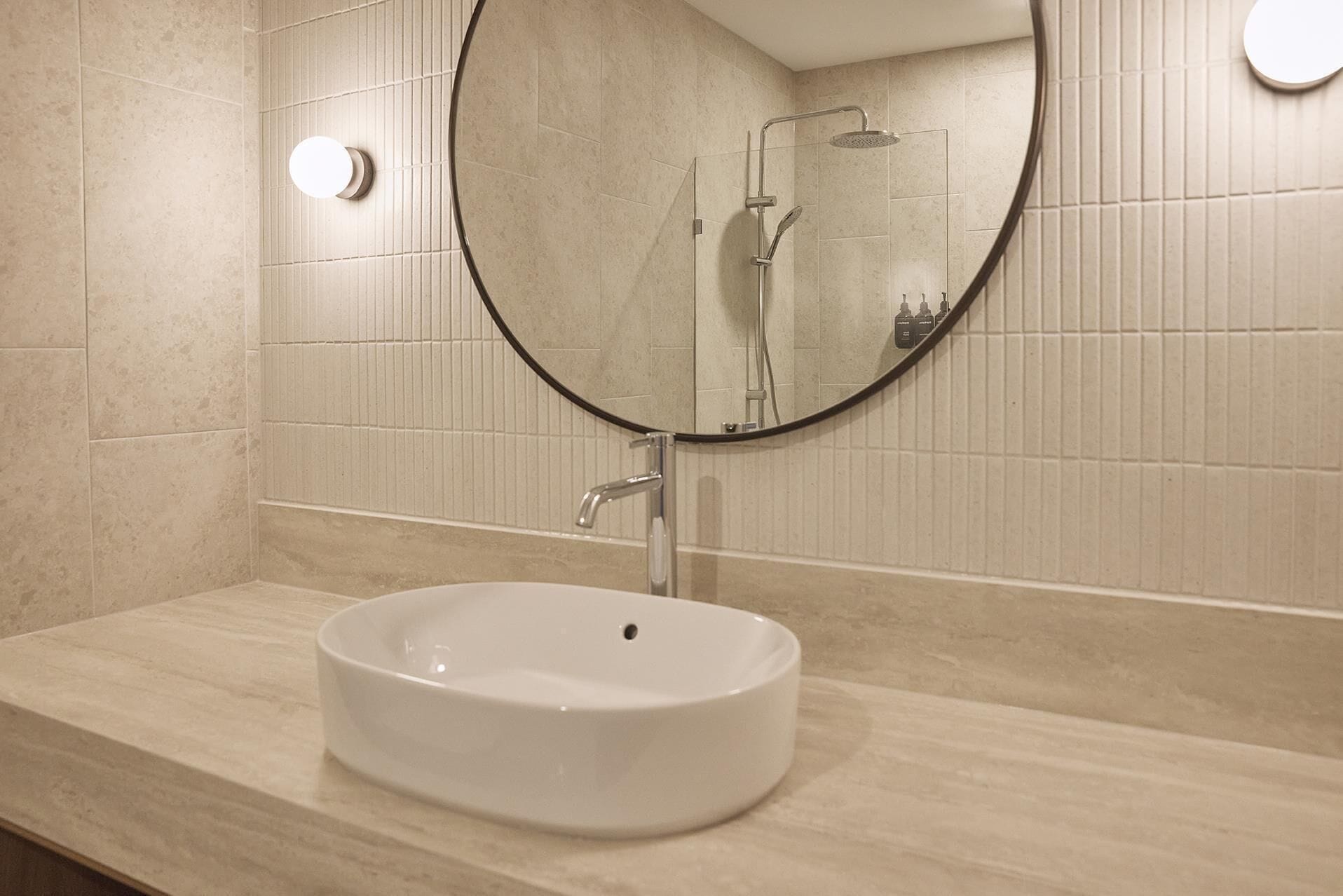 A bathroom with a round mirror, a white sink, and a shower.
