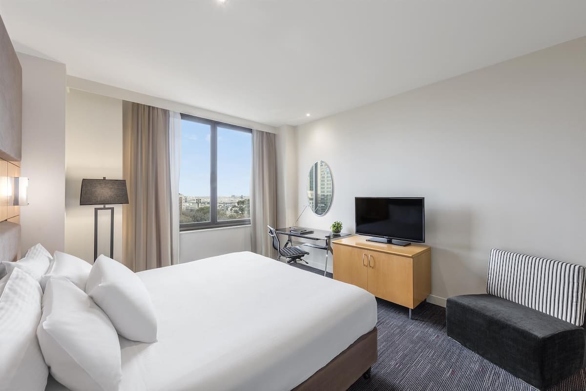 A hotel room with a bed, a desk, a television, a sofa, and a window with a view.